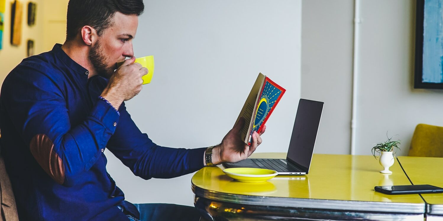 Homem tomando café enquanto lê um livro